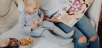Mother reading a book to her daughter in a cozy bedroom setting with snacks nearby.