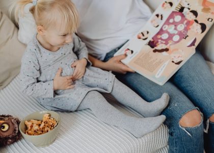 Mother reading a book to her daughter in a cozy bedroom setting with snacks nearby.