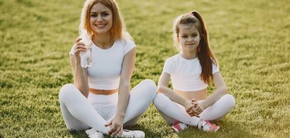 Smiling mother and daughter wearing matching outfits sitting on grass in a park.