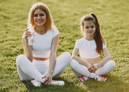 Smiling mother and daughter wearing matching outfits sitting on grass in a park.